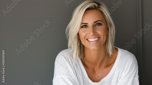 A confident, joyful woman in her middle age smiles warmly at the camera, radiating positivity against a grey backdrop.