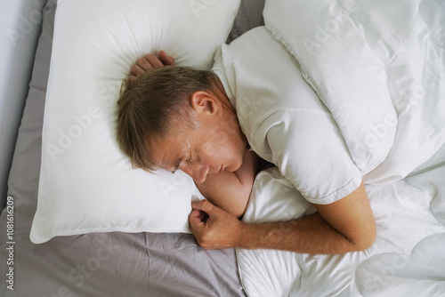 Man peacefully sleeping in a cozy bed with white bedding and a gray sheet during early morning hours photo