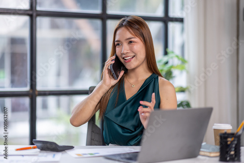 Cheerful business Asian woman freelancer making telephone call share good news about project working in office workplace, business finance concept.