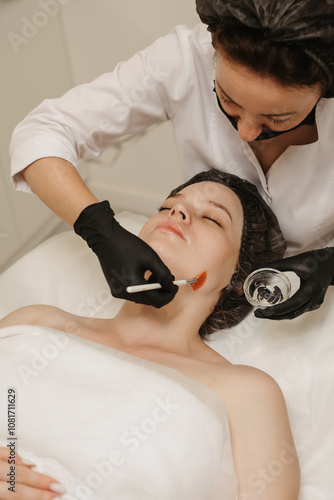 The cosmetologist applies a liquid gel to the face with a wide brush, the carboxytherapy procedure and its preparations. photo