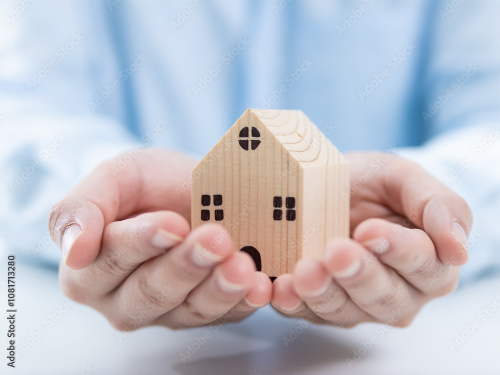 Supportive hands holding a wooden house model indoor setting family concept minimalist environment close-up view symbol of home and security Supportive hands holding a wooden house model indoor setting family concept minimalist environment close-up view symbol of home and security
