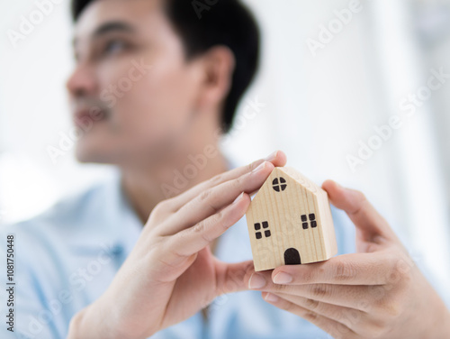 Creating a dream home a young man holding a wooden house model indoors modern workspace inspirational concept