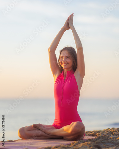 A smiling woman with freckles practices meditation in a lotus pose on a sandy beach at sunrise, promoting wellness, mindfulness, and inner joy. Ideal for yoga, meditation, and healthy lifestyle