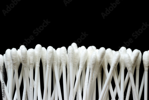 White cotton buds are stacked together on a black background.