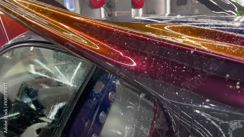 A specialist in wrapping a car with chameleon-colored vinyl film in the process of work. Car wrapping specialists cover the car with vinyl sheet or film. Car wrapping close-up. Selective focus.