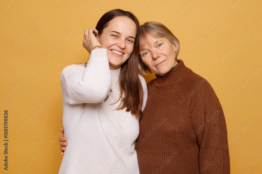 Two women stand closely together, smiling warmly against a bright yellow backdrop, showcasing their joyful connection and affection during a casual portrait session Two women stand closely together, smiling warmly against a bright yellow backdrop, showcasing their joyful connection and affection during a casual portrait session