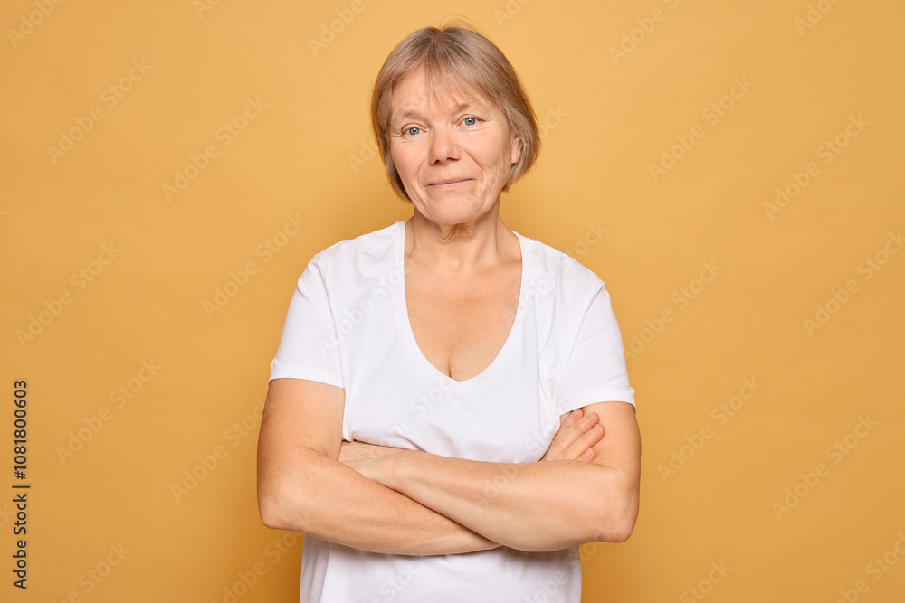 A woman in a simple white t-shirt stands confidently with her arms crossed against a vibrant yellow background, exuding strength and calmness A woman in a simple white t-shirt stands confidently with her arms crossed against a vibrant yellow background, exuding strength and calmness