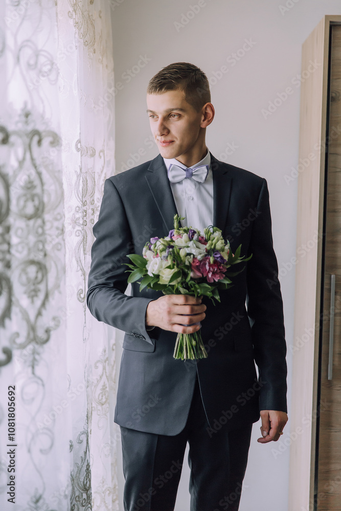 A man in a suit holding a bouquet of flowers. The man is wearing a bow tie and is standing in front of a window A man in a suit holding a bouquet of flowers. The man is wearing a bow tie and is standing in front of a window