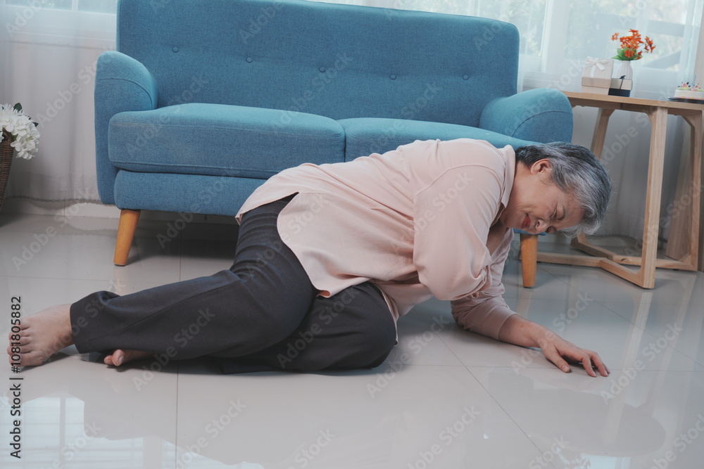An elderly woman with gray hair falls down on the floor of a room with shoulder pain, suffering from pain in her stomach in the living room at home.