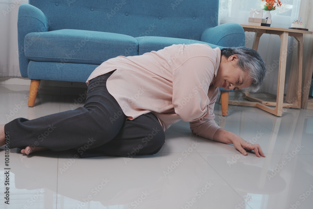 An elderly woman with gray hair falls down on the floor of a room with shoulder pain, suffering from pain in her stomach in the living room at home.