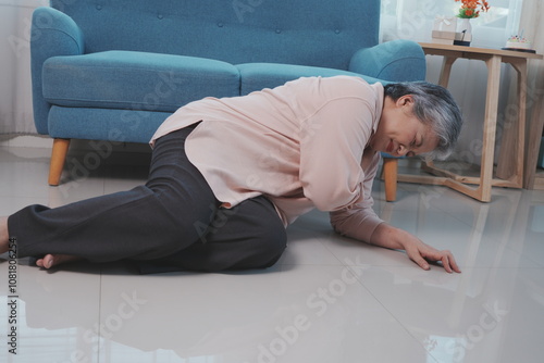 Obraz na płótnie An elderly woman with gray hair falls down on the floor of a room with shoulder pain, suffering from pain in her stomach in the living room at home. w salonie