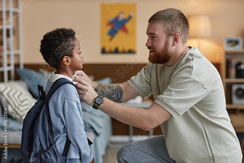 Fotografie Side view of happy adoptive father adjusting sons clothes while preparing little