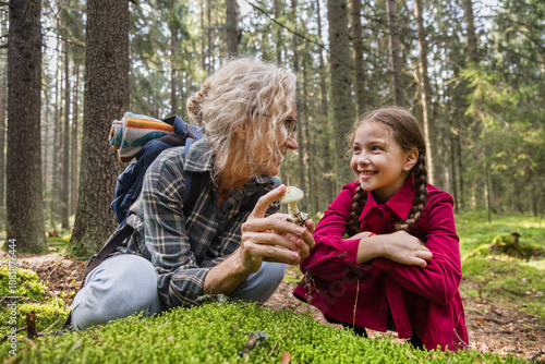 Little girl and grandmother looking at mushroom in forest photo