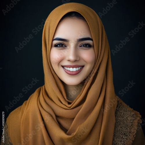 A young woman with brown eyes and a warm smile, wearing a mustard yellow hijab against a dark background.