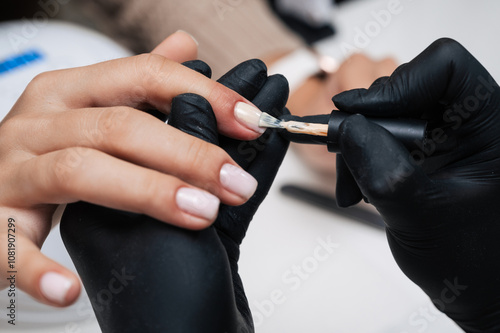 Manicure service. Close-up. Application of light varnish . The manicurist paints her nails with a transparent gel polish. Well-groomed nails. Professional salon hand care.