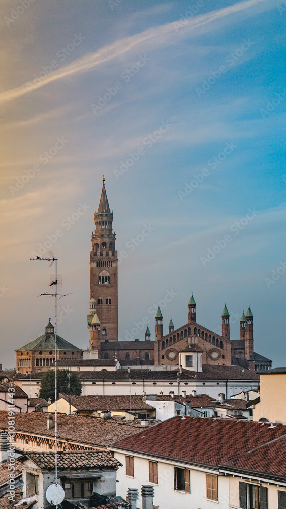 Naklejka premium Cremona duomo cathedral towers over the city, blending with rooftops and buildings against blue sky