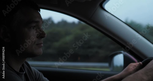 Wallpaper Mural Young man driving a car on a highway, surrounded by green trees and a serene landscape under an overcast sky Torontodigital.ca