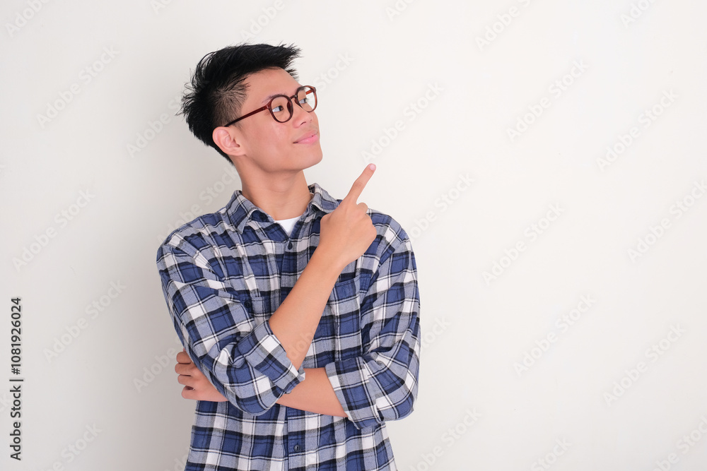 Young Asian man staring and pointing beside him with happy expression Young Asian man staring and pointing beside him with happy expression