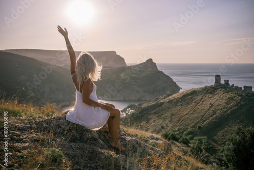Wallpaper Mural Happy woman is sitting on a hillside, wearing a white dress. She is surrounded by a beautiful landscape, with a body of sea in the background. Concept of peace and happiness. Torontodigital.ca