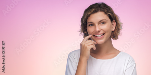 A smiling woman touches her chin with a finger against a pink gradient background. This high-quality stock photo is perfect for concepts of contemplation, positivity, and thoughtful moments in