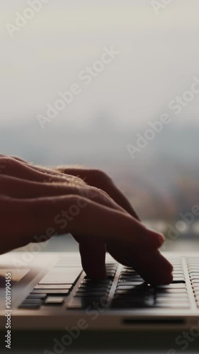 Close up of female fingers typing on keyboard against big window. Vertical video