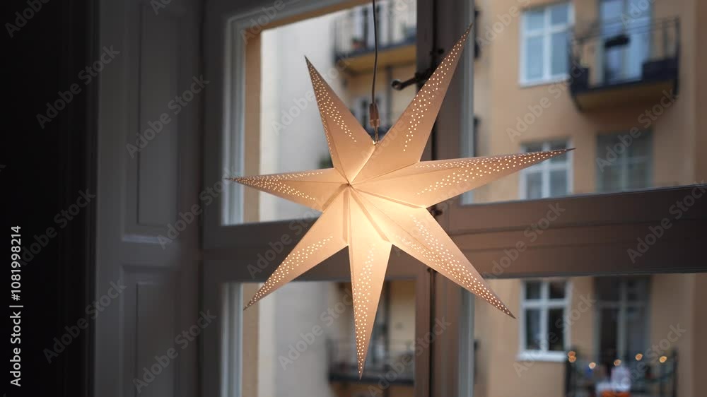 White lit paper star Christmas light in window facing old apartment building