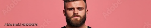 Young man with a beard posing against a pink background