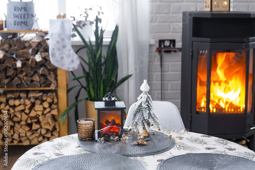 Metall black stove, burning hearth fireplace in white Festive interior of house is decorated for Christmas and New Year, Christmas tree. firewood in the woodpile, cozy and heating of home photo