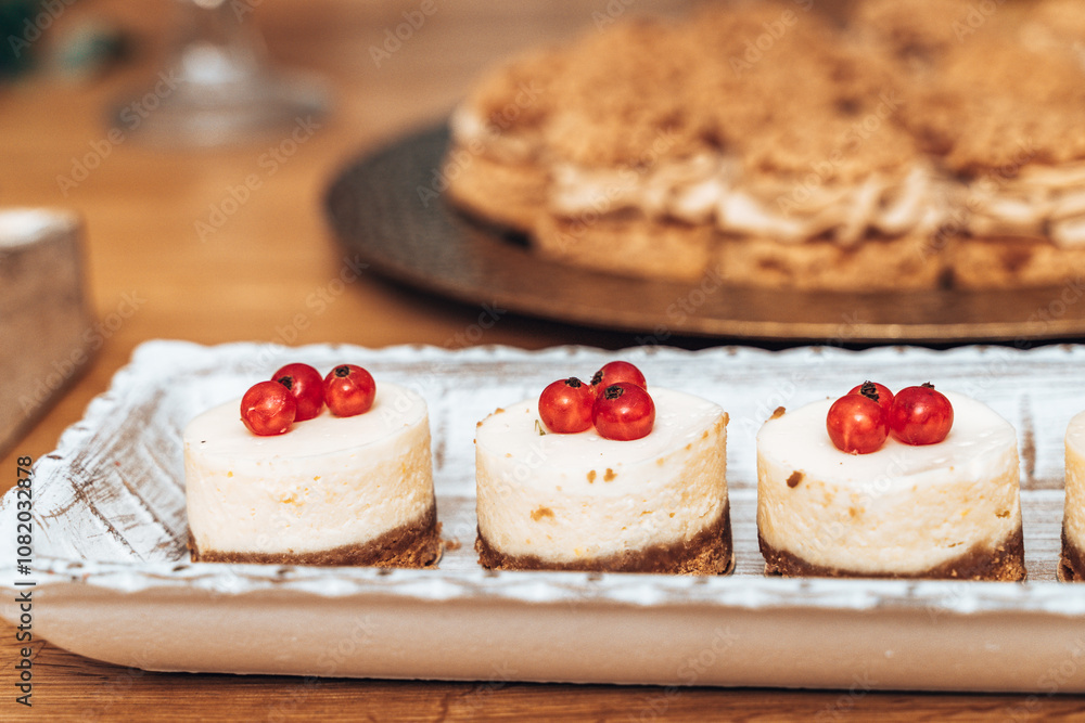 Mini cheesecakes with a smooth texture, each topped with a trio of vibrant red currants. Presented on a rustic ceramic tray, these bite-sized treats have a light, creamy finish over a crumbly crust.
Mini cheesecakes with a smooth texture, each topped with a trio of vibrant red currants. Presented on a rustic ceramic tray, these bite-sized treats have a light, creamy finish over a crumbly crust.