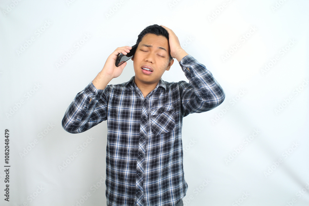 unhealthy asian man with migraine and fatigue calling health care using smartphone isolated on white wearing casual shirt unhealthy asian man with migraine and fatigue calling health care using smartphone isolated on white wearing casual shirt
