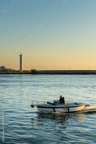 Viareggio, Lucca, Italy: the port at sunset with a fishing boat returning and the lighthouse in the background