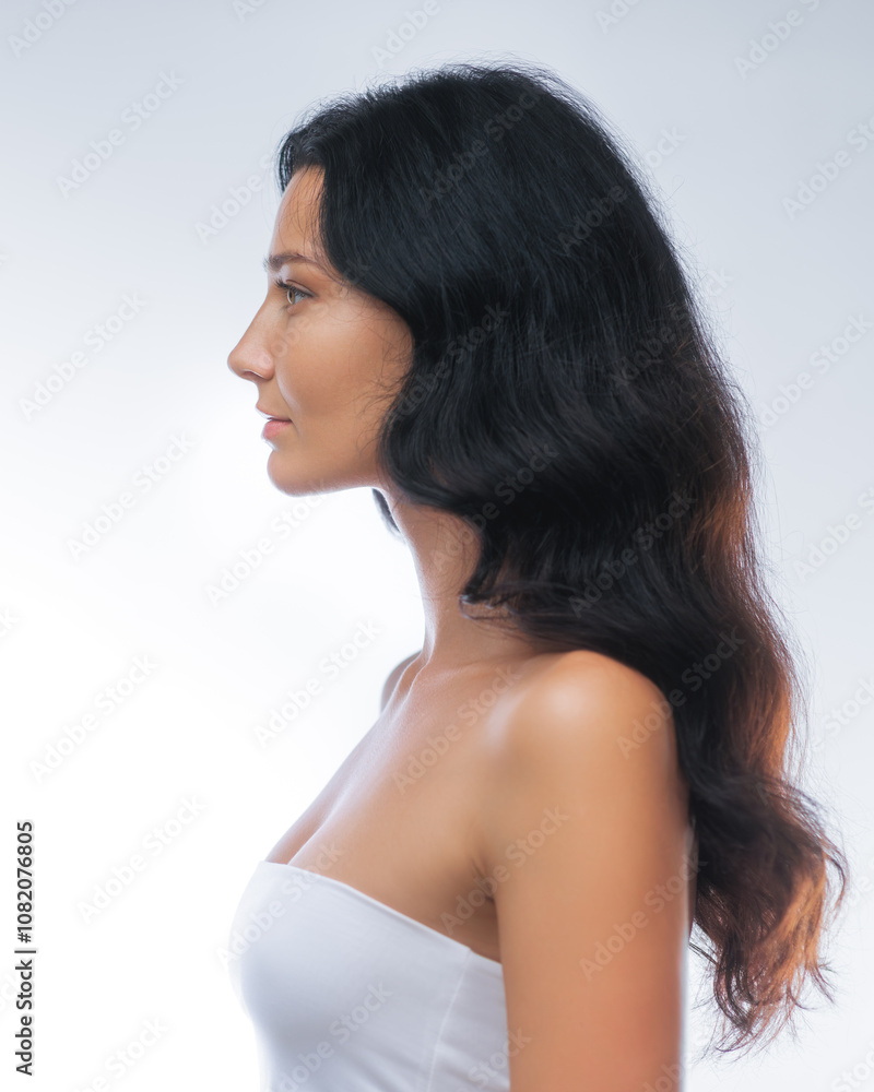 Side profile of a young woman with long dark hair and clear skin, wearing a white top against a clean white background. Ideal for beauty, skincare, and wellness concepts in minimalist design. Side profile of a young woman with long dark hair and clear skin, wearing a white top against a clean white background. Ideal for beauty, skincare, and wellness concepts in minimalist design.