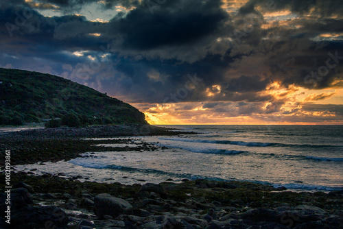 Dramatic sunset over rocky shore of Pacific Ocean near Raglan, New Zealand