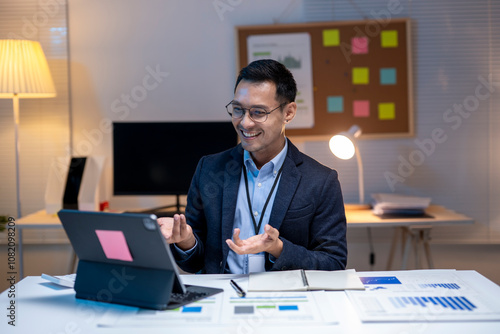 Asian businessman making video call using tablet in office at night