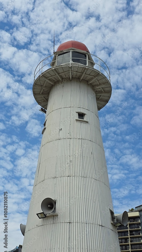 White painted metal lighthouse with a red roof against a blue sky with white clouds White painted metal lighthouse with a red roof against a blue sky with white clouds