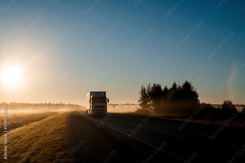 A truck drives along the highway at dawn through the fog A truck drives along the highway at dawn through the fog