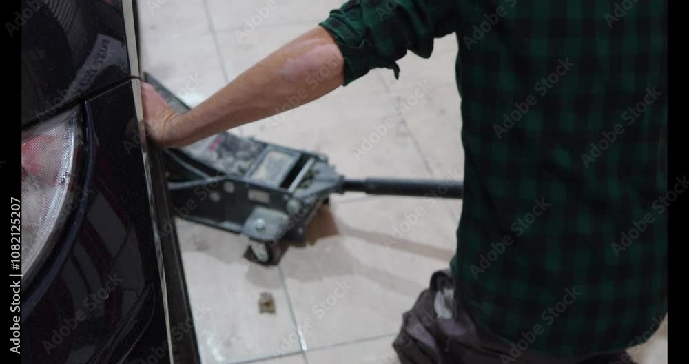Mechanic lifting a car with a hydraulic jack in a workshop Mechanic lifting a car with a hydraulic jack in a workshop