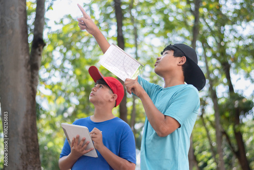 Asian schoolboys are studying high level of trees in school botanical garden by using inclinometer and measure tape and looking up for measuring high level of trees and saving information into taplet. photo