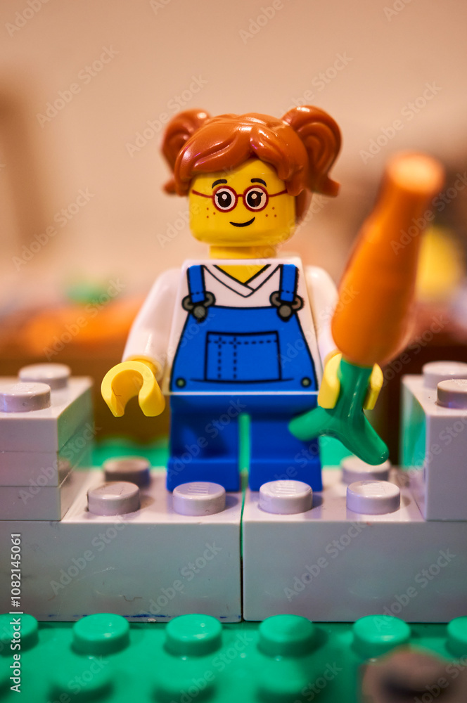 Fototapeta premium Vertical closeup of a Lego small girl toy figurine holding a carrot