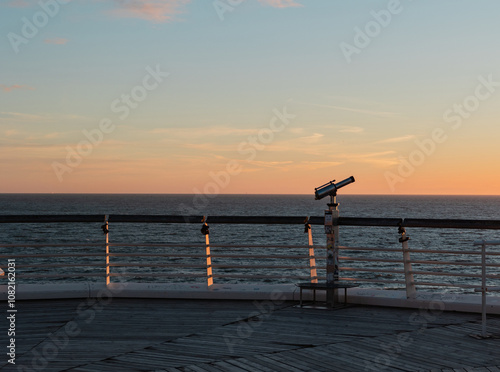 Binoculars at the edge of the pier in Scheveningen. Sunset, warm light, tranquil scene. The Hague, Netherlands.