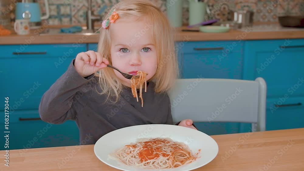 Little child toddler girl Caucasian eats spaghetti with tomato sauce with a fork, at home in the kitchen, sstkBabies Little child toddler girl Caucasian eats spaghetti with tomato sauce with a fork, at home in the kitchen, sstkBabies