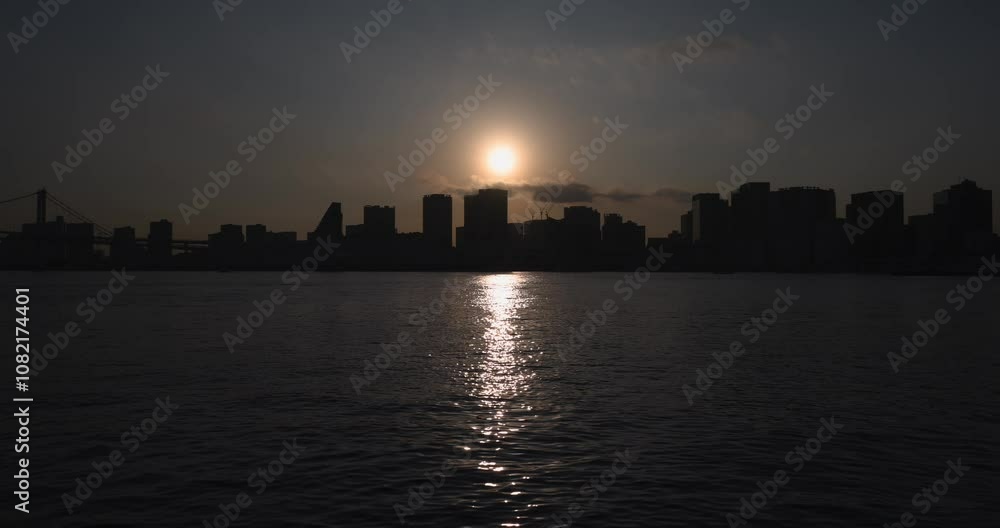 ビルの上に沈む太陽の光が海面に反射している風景。 ビルの上に沈む太陽の光が海面に反射している風景。