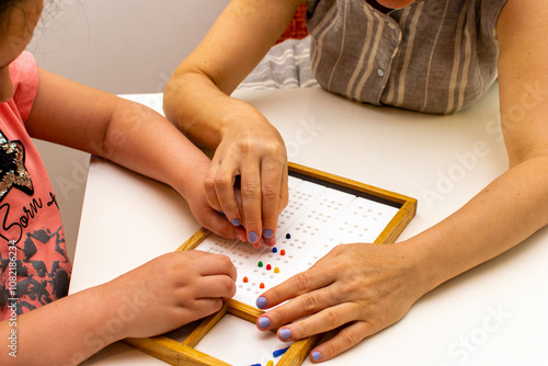 The hands of a girl and the hands of a teacher in close-up. Braille board for learning alphabet. photo