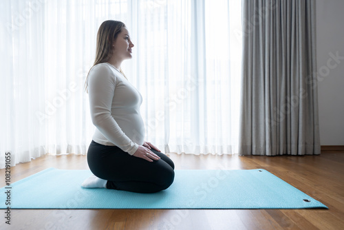 Gen Z pregnant woman sitting on yoga mat at home. Workout, yoga and fitness at home, pregnancy concept. Pre-natal.