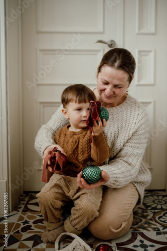 Grandmother and grandson in beige knitted sweaters look at vintage Christmas balls. Preparation for Christmas