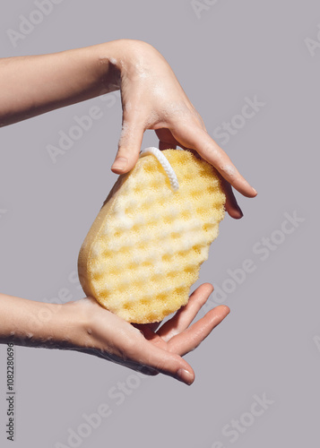 woman holds a foamed yellow washcloth in her hands 