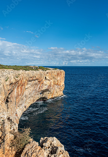 Landscape photography of rock climbing cliff, rocky coast; tourist destination; blue sky with clouds, boulders; rocks; travel; Mallorca; Spain; Porto Cristo, Cova del Diablo