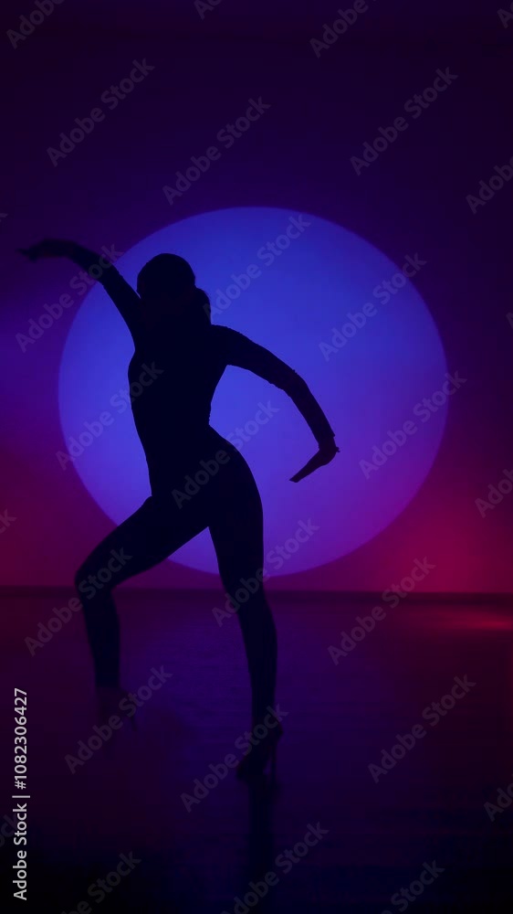 Silhouette of a woman dancing in blue neon light.Woman dancing dance in a blue light circle.Dance and movement concept.Vertical video