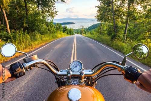 A motorcycle rider enjoys a scenic drive on a winding road with a lake in the distance.
