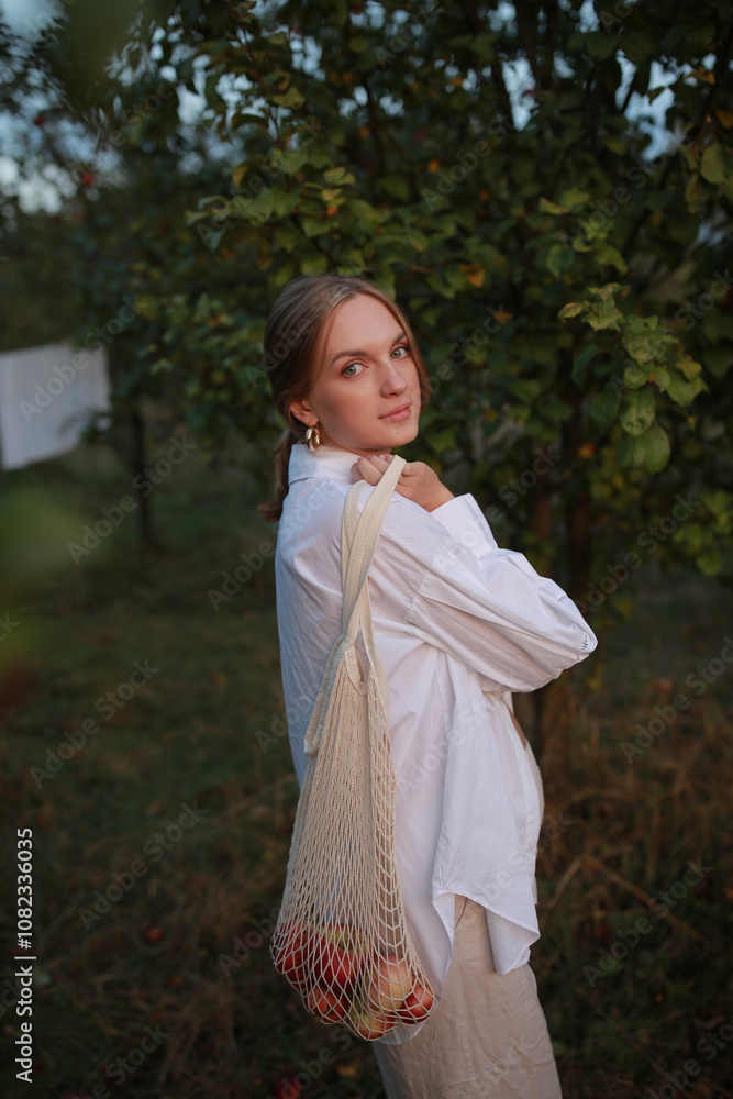woman with a string bag, containing apples. pregnant woman picking apples in the garden. girl holding a bag string with apples. Harvesting. Autumn. Apple orchard. Zero waste concept. Outdoors woman with a string bag, containing apples. pregnant woman picking apples in the garden. girl holding a bag string with apples. Harvesting. Autumn. Apple orchard. Zero waste concept. Outdoors